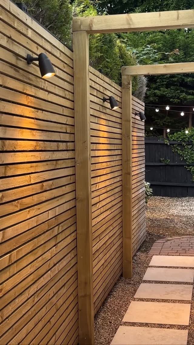 Rectangular stone pavers form a walkway path alongside a modern wooden slat fence.