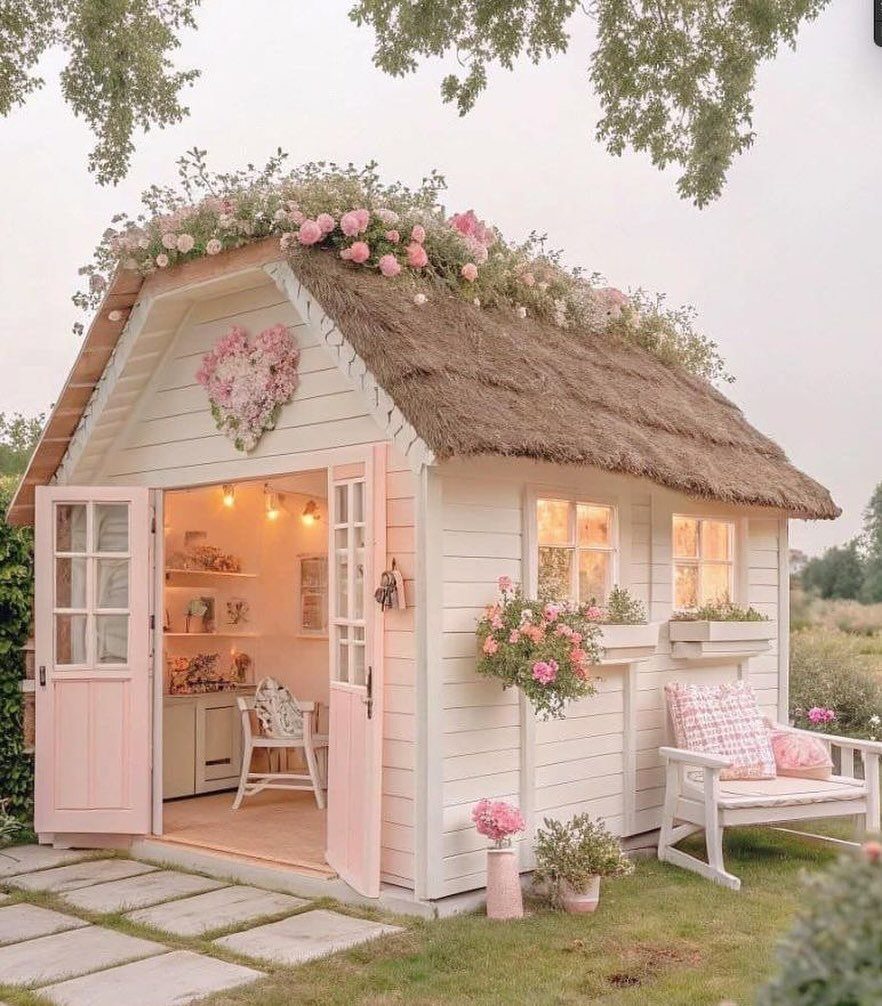A small white cottage with a thatched roof and pink rose decorations in a garden.