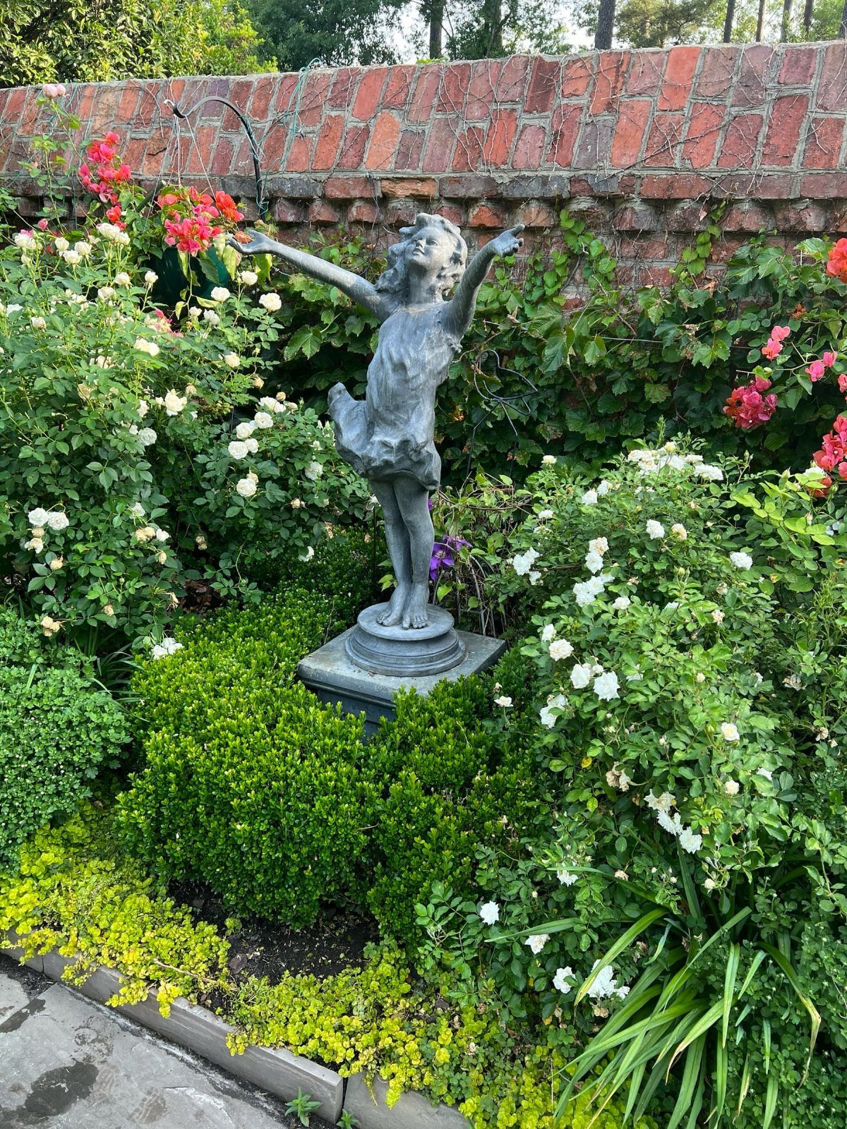 17 Small Front Yard Landscape Ideas with Photo Inspiration 8 A stone statue of a girl with arms outstretched amidst blooming white roses and green shrubs.