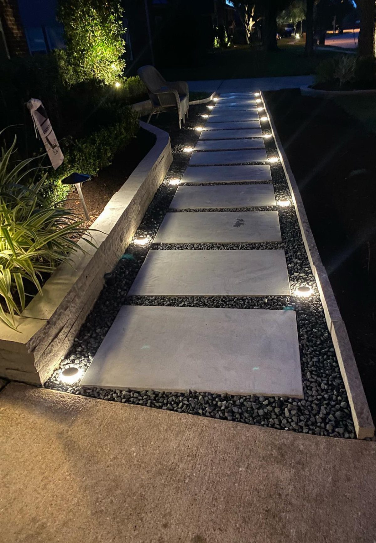 17 Small Front Yard Landscape Ideas with Photo Inspiration 6 Large rectangular stone pavers set in dark gravel with integrated pathway lighting at night.