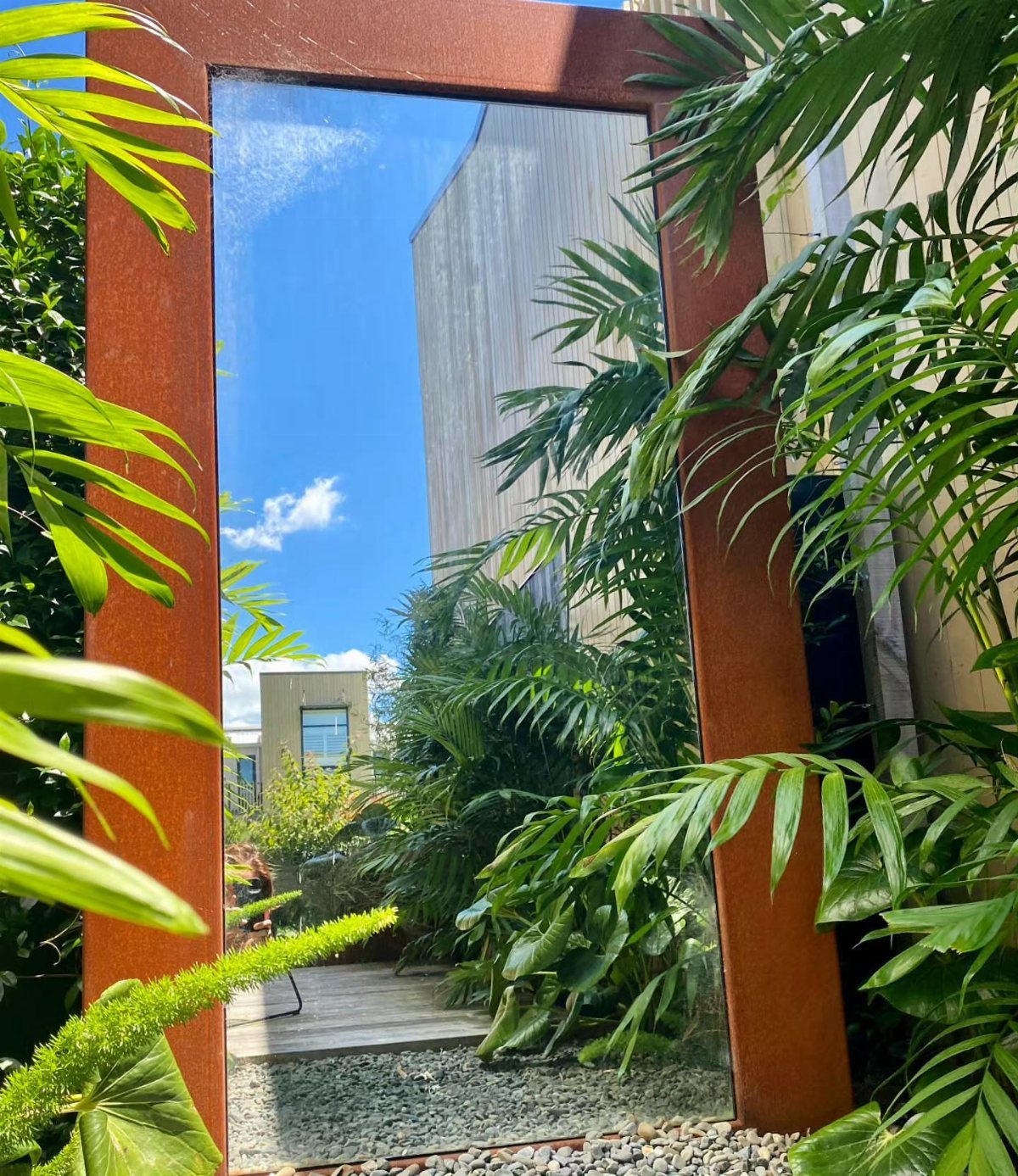 17 Small Front Yard Landscape Ideas with Photo Inspiration 7 A large rectangular garden mirror with a rusted frame reflects the blue sky and greenery.