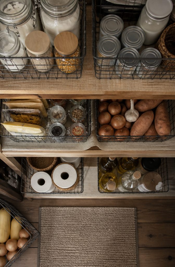 Wire and mesh baskets on pantry shelves containing various food items.