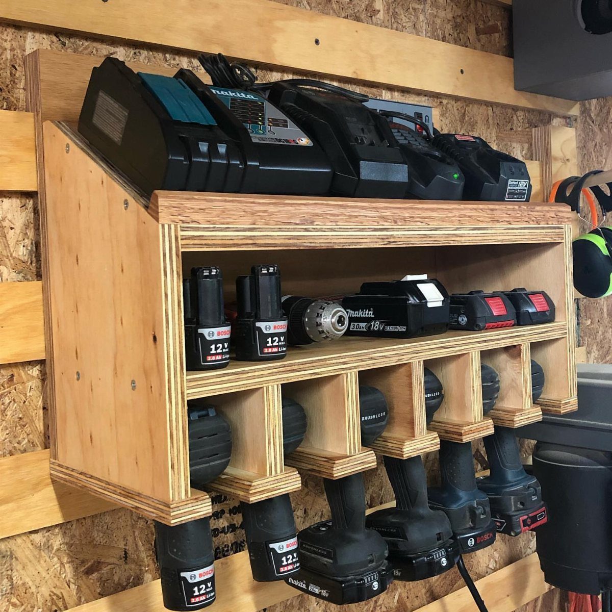 Wooden wall-mounted charging station holding various cordless drill batteries and power tools.