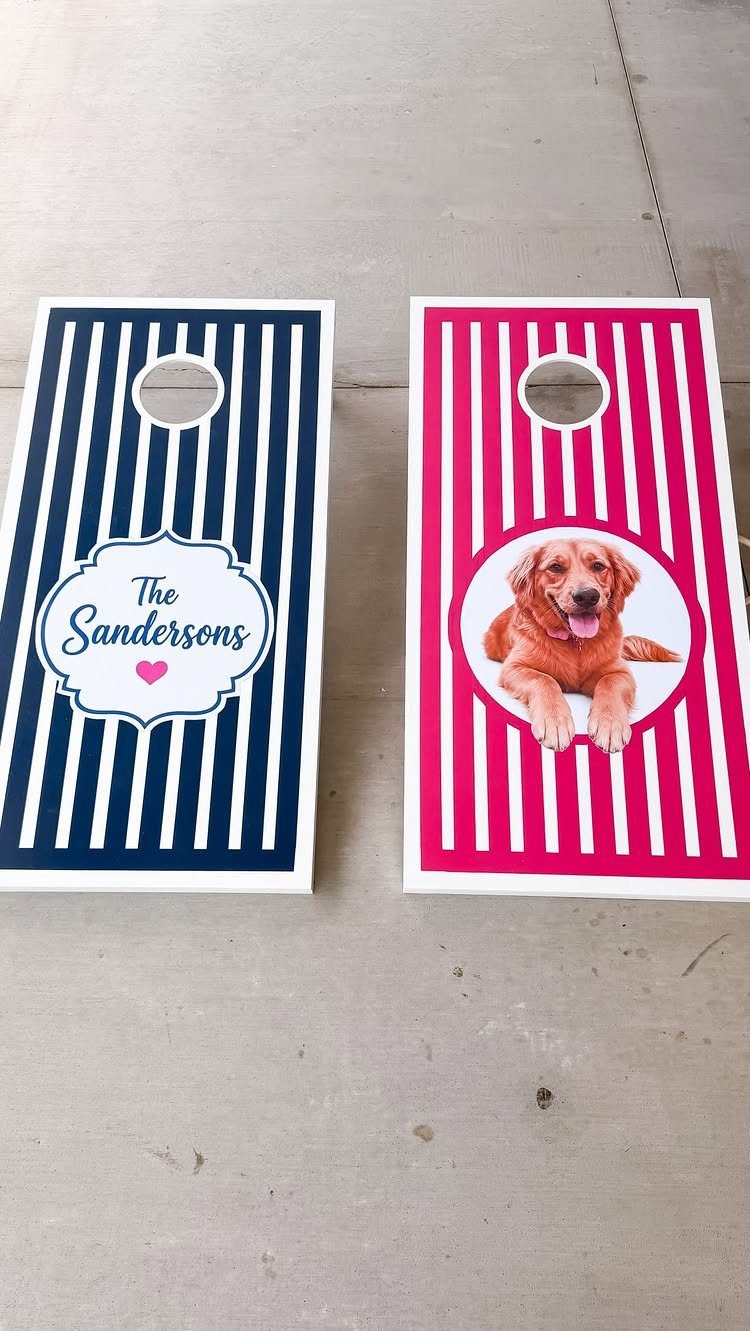 Two custom striped cornhole boards with a nameplate and a dog photo on concrete.