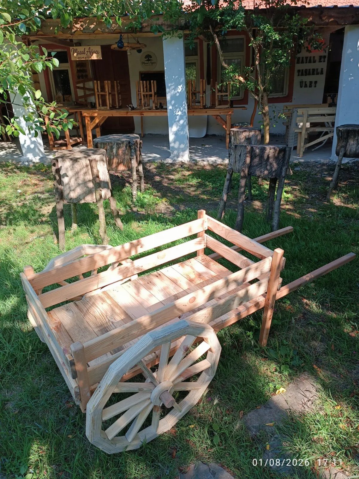 A small wooden garden cart with large spoked wheels sitting on a grassy yard.