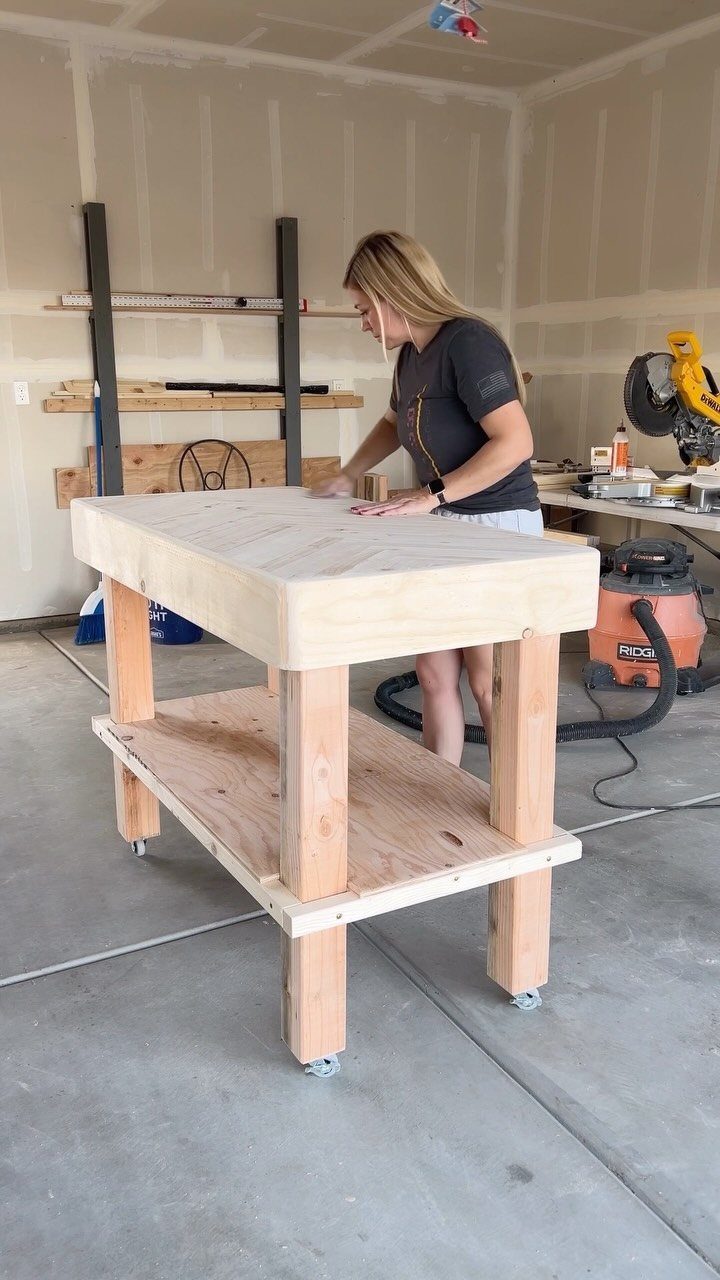 A woman works on a newly built wooden workbench with wheels in a garage.