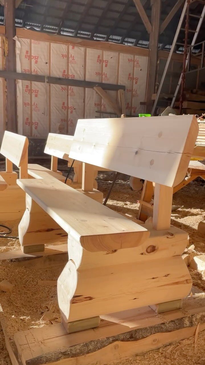 Several unfinished light-colored wooden benches resting on a sawdust-covered workshop floor.