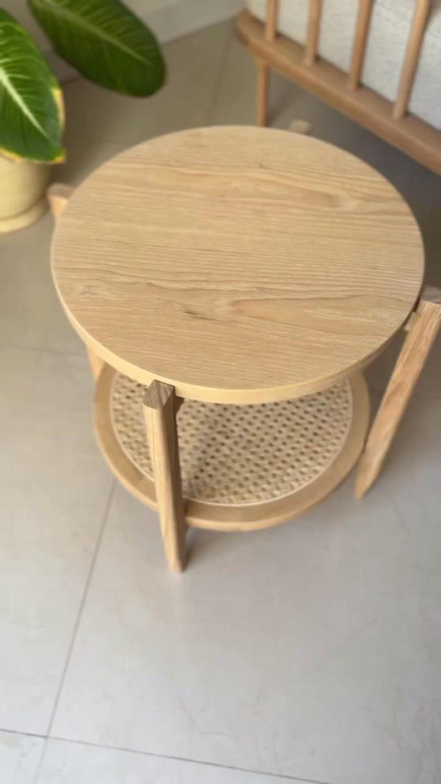 A two-tier round wooden side table with a woven cane bottom shelf.