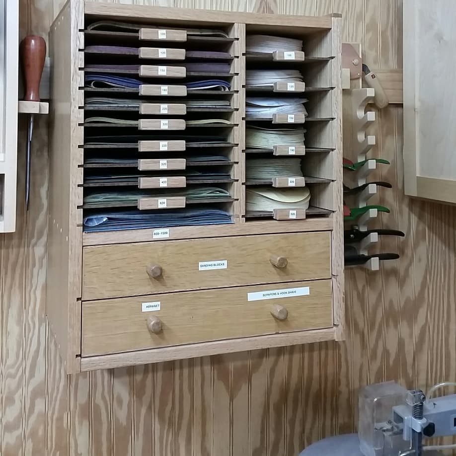 Wooden wall-mounted organizer filled with various sandpaper discs and two small storage drawers.