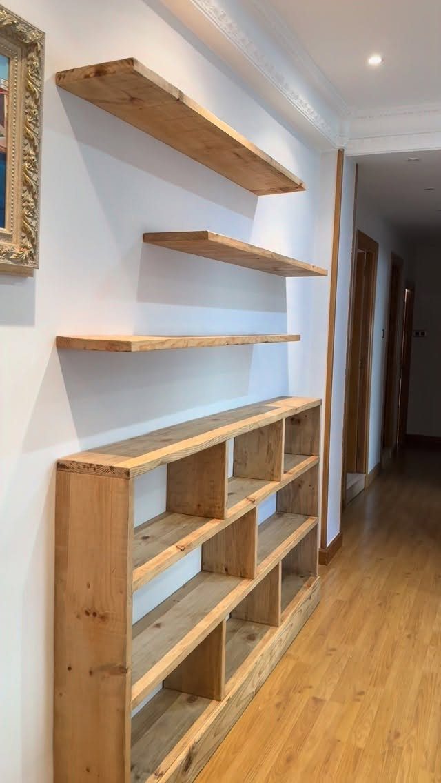 Three rustic wooden floating shelves mounted on a white wall above a large wooden bookshelf.