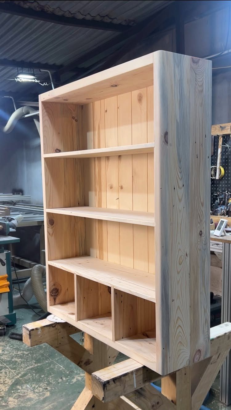 A tall light wood shelving unit resting on a wooden sawhorse in a workshop.