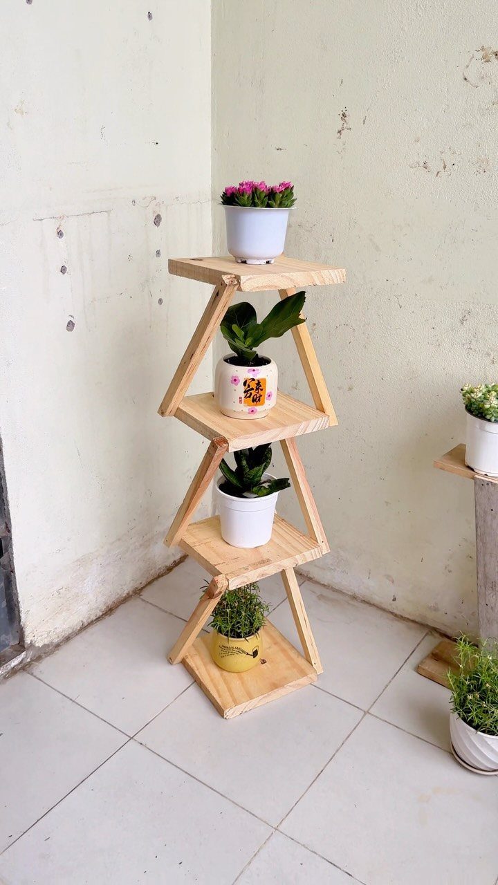 A tiered wooden plant stand holding three small potted plants against a white wall.