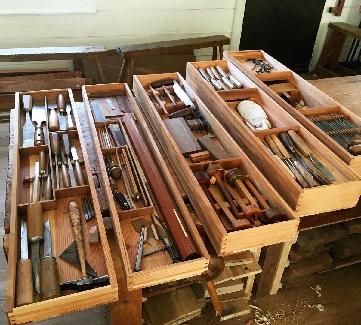 Multiple wooden tool trays filled with various woodworking hand tools on a workbench.