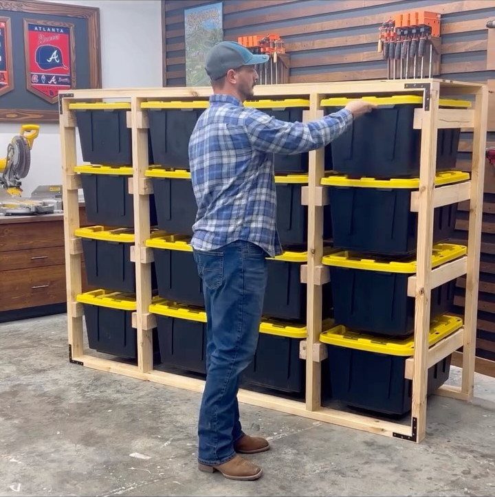 A man reaches into a large wooden storage rack filled with black and yellow plastic bins.